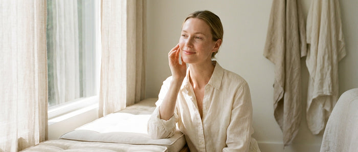 Woman with calm glowing skin touching her face near a window — sensitive skin care